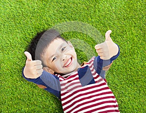 Smiling kid lying and thumb up on a meadow