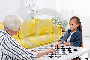 Smiling kid playing checkers with blurred