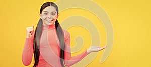 smiling kid presenting product, copy space. pretty teen girl advertising on yellow background. Child face, horizontal