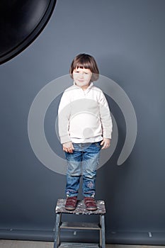 Smiling kid standing up on dirty stool at photoshooting session