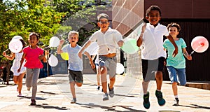 Smiling kids with balloons running in race and laughing at street