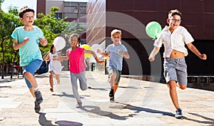 Smiling kids with balloons running in race and laughing at street