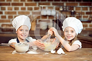 Smiling kids in chef hats making dough for cookies