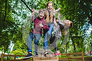 Smiling kids having fun at playground. Children playing outdoors in summer. Teenagers riding on a swing outside