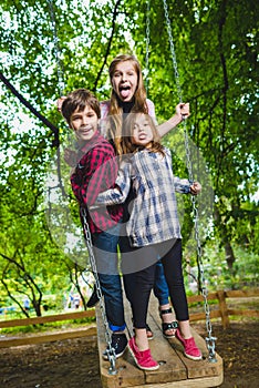 Smiling kids having fun at playground. Children playing outdoors in summer. Teenagers riding on a swing outside