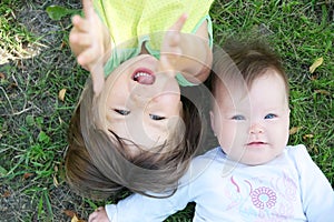 Smiling kids lying on grass in summer. Children: Toddler and baby portrait having fun. Little sisters. Happy childhood