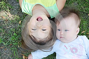 Smiling kids lying on grass in summer. Children: Toddler and baby portrait having fun. Little sisters. Happy childhood