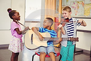 Smiling kids playing guitar, violin, flute in classroom