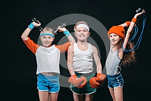 Smiling kids in sportswear posing with sport equipment and looking at camera