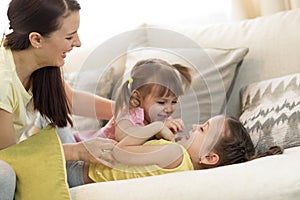 Smiling kids and their mom having a fun pastime together on couch in living room at home