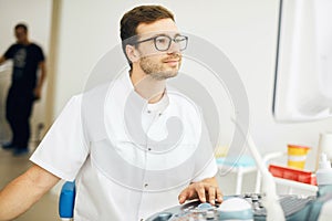 Smiling kind doctor looking at the computer and using the ultrasound machine