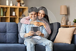 Smiling korean couple websurfing on tablet gadget at home