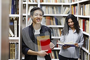 Smiling korean guy holding textbooks at campus library