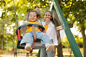 Smiling Korean Mother Swinging Baby On Swing On Playground