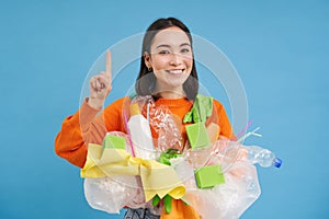 Smiling korean woman pointing up, showing recycling eco banner, holding recycle waste, sorting garbage at home, isolated