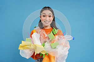 Smiling korean woman, recycling, holding plastic waste and sorting it for recycle center, blue background