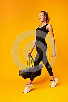 Smiling Lady Carrying Gym Bag With Rolling Mat, Yellow Background