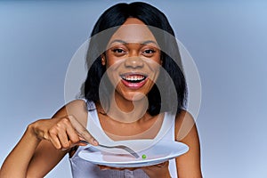 Smiling lady on a diet eating the last pea from the empty white plate. Diet concept
