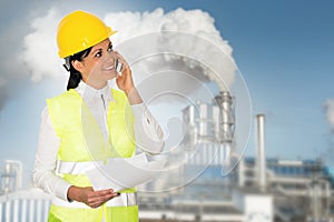 Smiling lady engineer talking on the phone and the factory in th