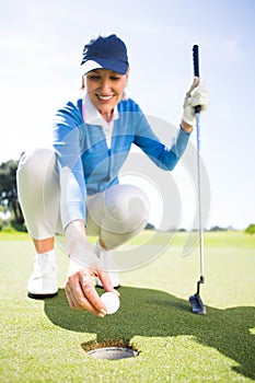 Smiling lady golfer kneeling on the putting green