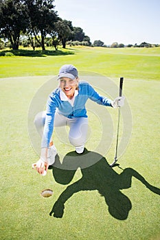 Smiling lady golfer kneeling on the putting green