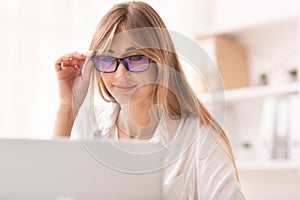 Smiling Lady Looking Through Eyeglasses At Laptop Working In Office