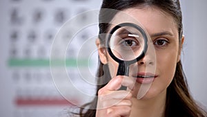 Smiling lady looking through magnifying glass, eye cornea genetics, treatment