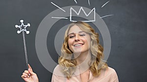 Smiling lady with magic wand standing near chalkboards with crown drawing, fun