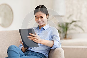 Smiling lady sitting on sofa, using digital tablet