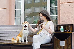 Smiling lady stroking beautiful dog and holding cup of coffee in street cafe