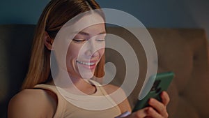 Smiling lady texting mobile phone in bed at evening close up. Woman chatting