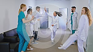 Smiling large group of nurses and doctors dancing excited in front of the camera in a modern hospital corridor they are