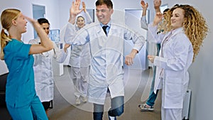 Smiling large group of nurses and doctors dancing excited in front of the camera in a modern hospital corridor they are