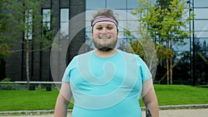 Smiling large posing obese young man in front of the camera he prepares to start the aerobic workout outside beside a