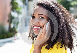 Smiling latin woman with curly hair at phone in summer