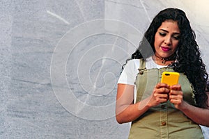 Smiling latin woman with curly hair at phone in summer