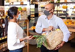 Smiling Latino in protective mask talking to woman in grocery store