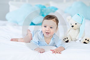 Smiling or laughing baby on the bed to sleep with teddy bear, baby room interior, healthy happy little baby