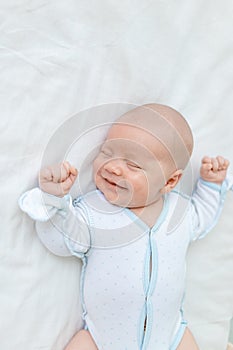 Smiling or laughing in a dream, a newborn baby boy sleeps for seven days in a cot at home on a cotton bed, close-up