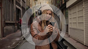 Smiling and laughing handsome young woman girl listening music from his smartphone in headphones, dancing on street of