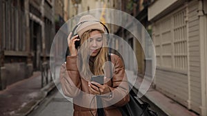 Smiling and laughing handsome young woman girl listening music from his smartphone in headphones, dancing on street of