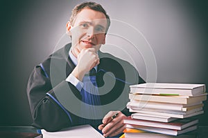 Smiling lawyer in a gown sits at a desk full of books