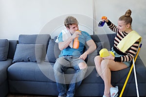 Smiling and lazy Young Caucasian couple love husband and wife funny and relaxing with Spray together on sofa for housework in