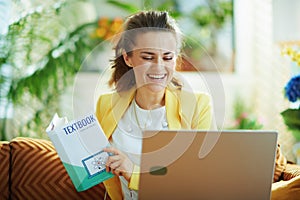 Smiling learner woman with laptop and textbook study online