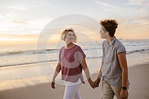 Smiling lesbian couple walking along a beach at sunset