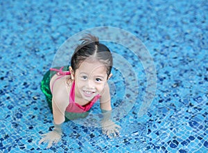 Smiling little Asian child girl in a mermaid suit playing poolside with looking camera