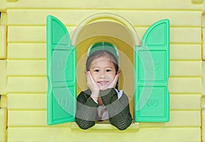 Smiling little Asian child girl playing with window toy playhouse in playground