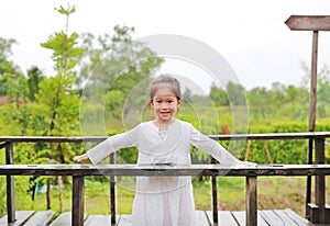 Smiling little Asian child girl posting open arms on wood bridge at the nature