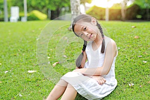 Smiling little Asian child girl with two ponytail hair lying on green grass in the garden