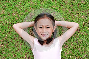 Smiling little Asian child girl with two ponytail hair lying on green grass in the garden